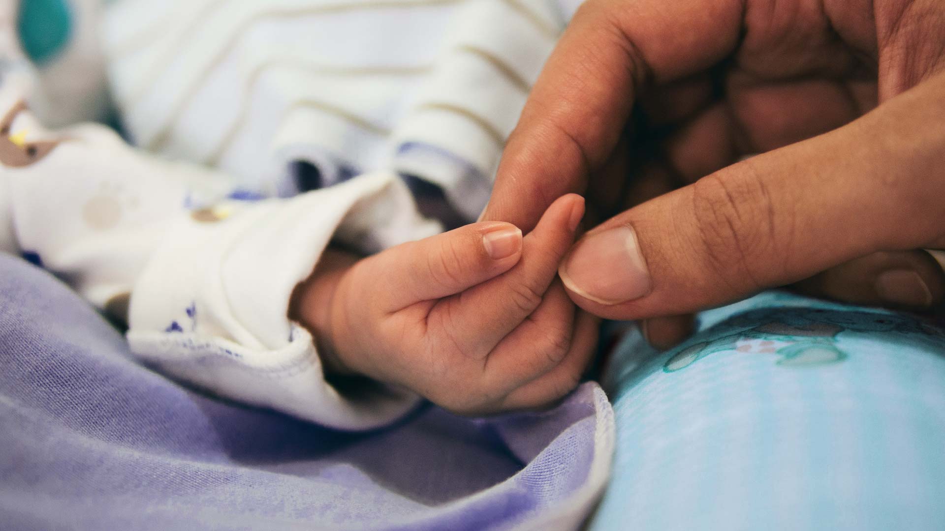 Close-up of a baby and mother holding hands, the photograph has been treated with Luvvi brand colours.